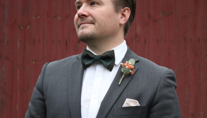 edvin-rusetti Mies harmaassa puvussa, tummanvihreä käsintehty nahka–tweed-rusetti kaulassaan.