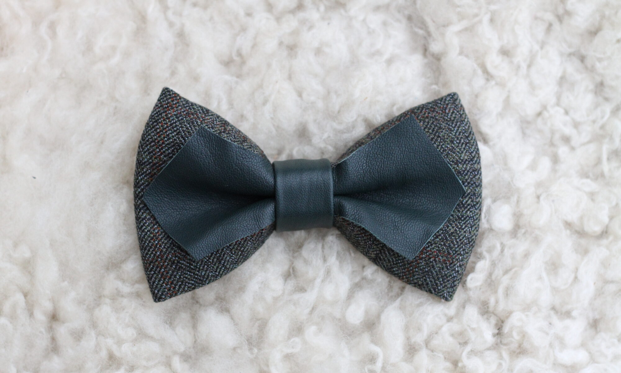 Käsintehty tummanvihreä nahka-tweed-rusetti vaalealla taustalla.