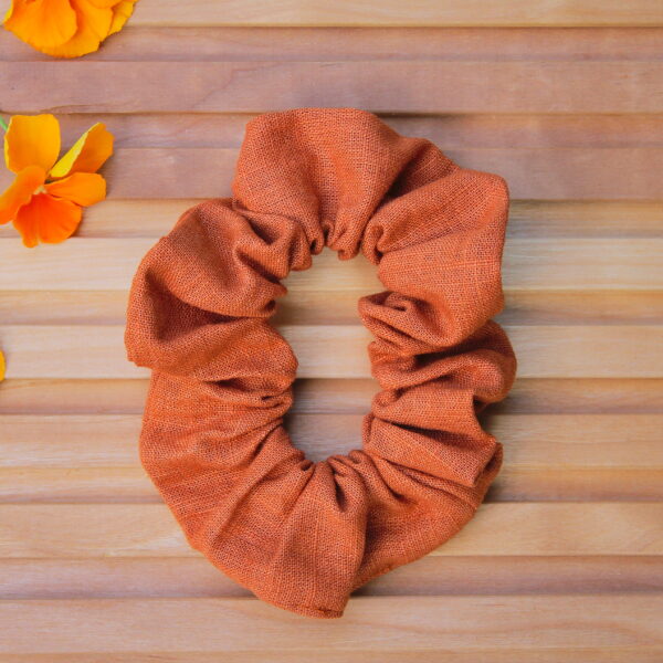 Pellavainen hiusdonitsi lämpimän kanelin sävyssä puupintaisella taustalla, vieressä oransseja orvokkeja.