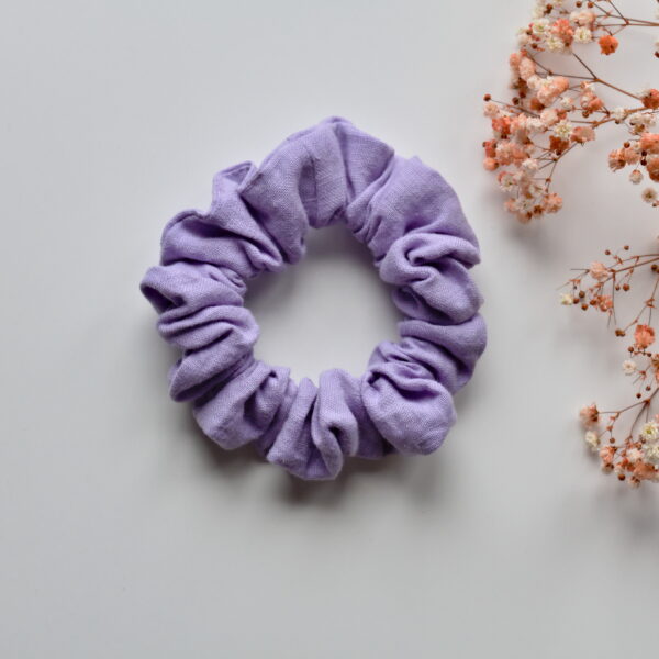 Kuvassa valkoista taustaa vasten pellavainen vaalean liilan sävyinen hiusdonitsi. Taustalla kuivakukkia.