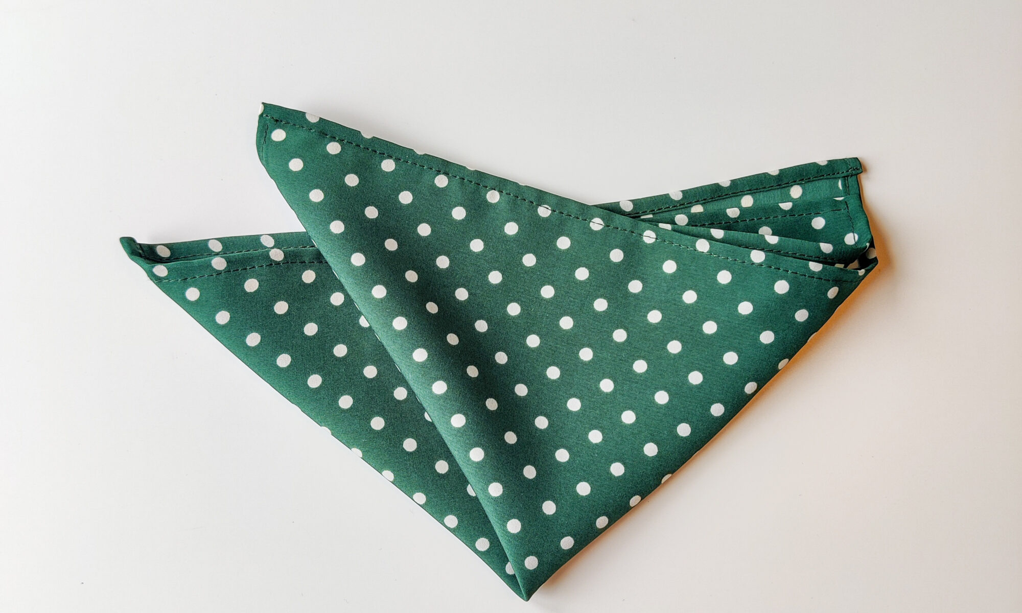 Kuvassa tumman vihreä valkoisilla pilkuilla taiteltu taskuliina